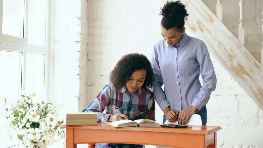 A member of staff supporting a young person with their work at a desk